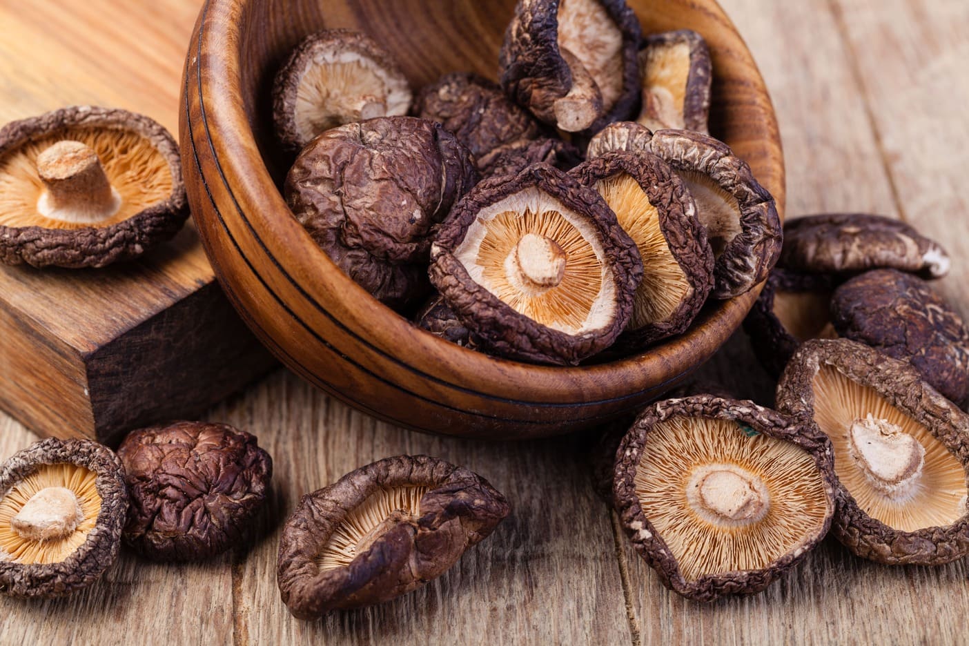 Dried Shitake mushrooms in a wooden bowl on a wooden surface