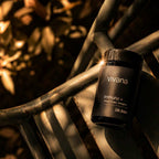 A black jar of vivana Immuno+ Life Baler supplement placed on a dark metal bench in warm, dramatic sunlight with blurred foliage in the background.